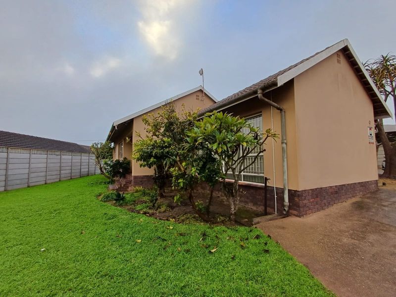 Rear view of the house featuring a tiled roof, brick plinth, security bars on windows, and a concrete driveway adjacent to a lawn.