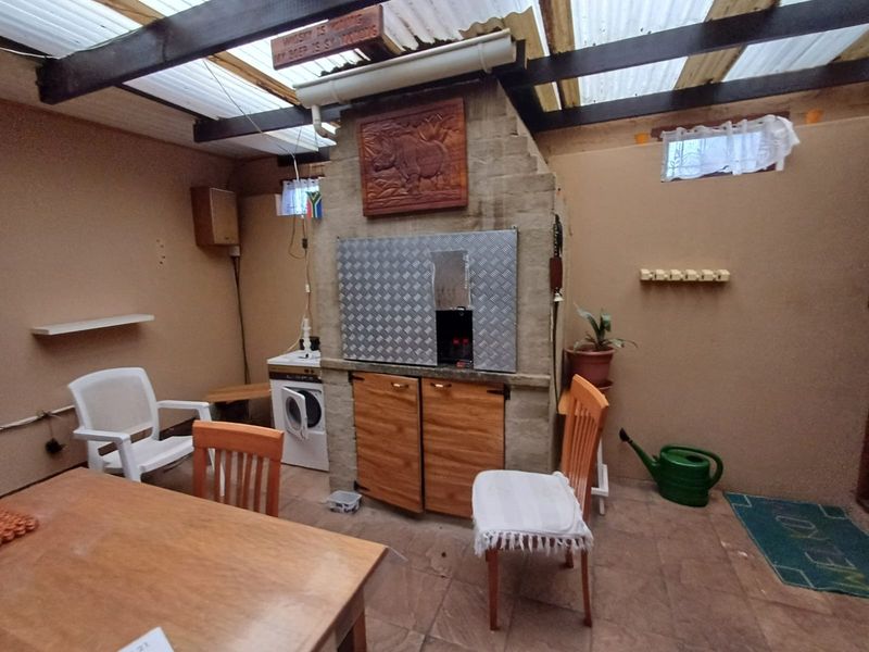 Covered patio area featuring a built-in braai, corrugated roof structure, and tiled flooring, offering a functional outdoor entertainment space.