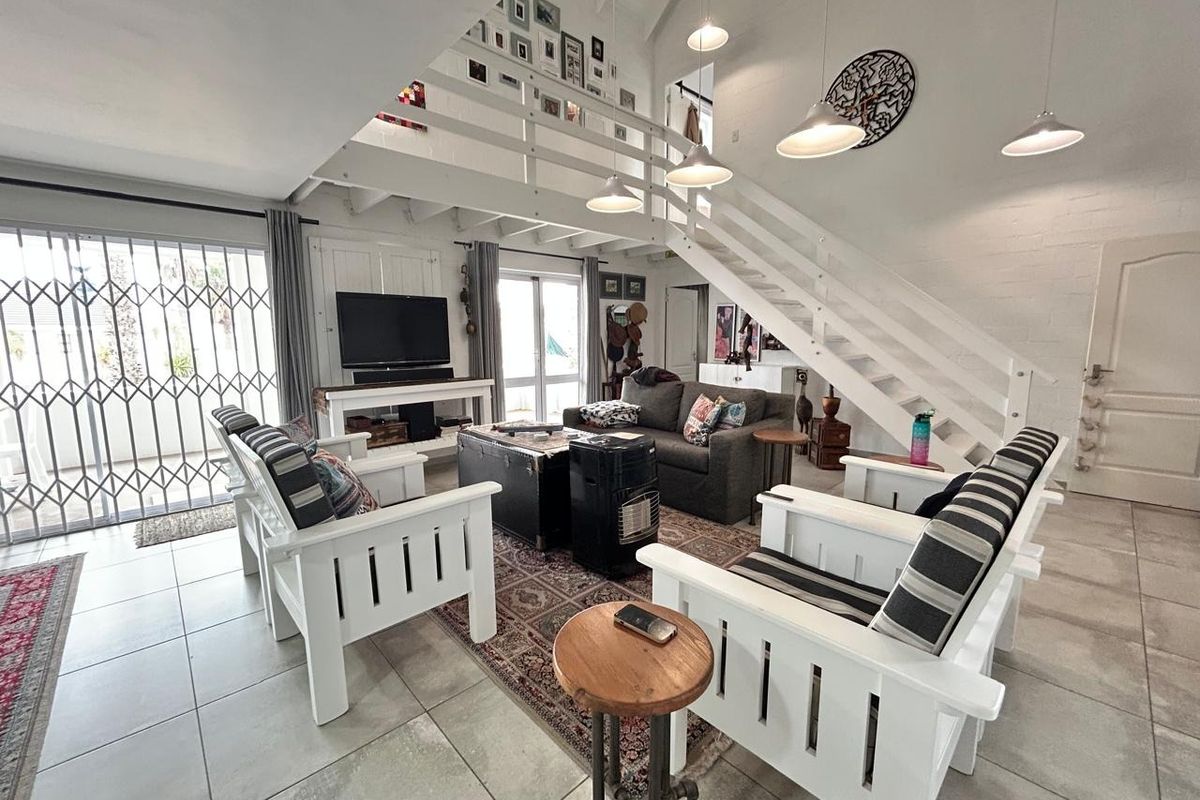Spacious open-plan living area featuring a mezzanine level, timber staircase, tiled flooring, and abundant natural light through large glass doors.
