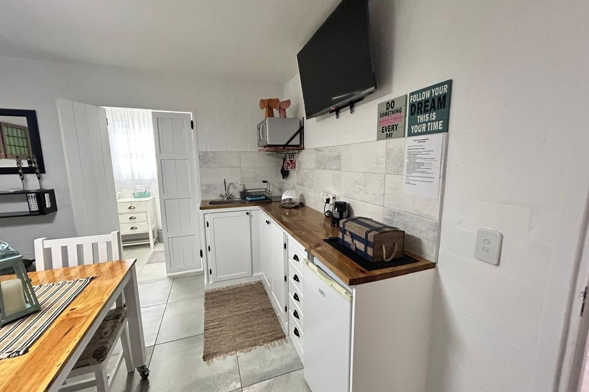 A compact kitchen area featuring white cabinetry, wooden countertops, a tiled backsplash, and tiled flooring, with an adjacent doorway leading to another room.