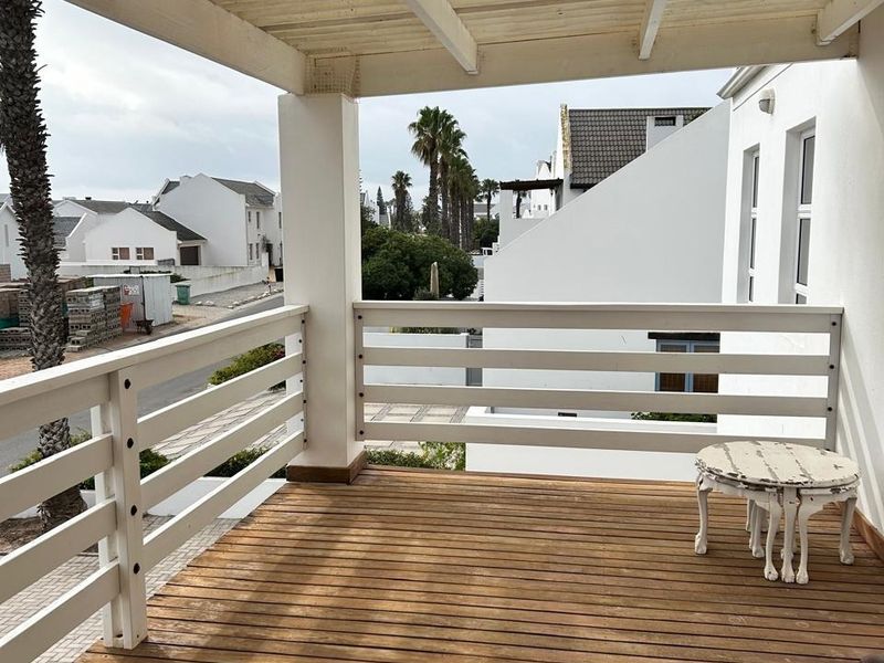 A covered balcony featuring timber decking and a white timber pergola, offering an open outdoor space with views of the surrounding neighborhood.