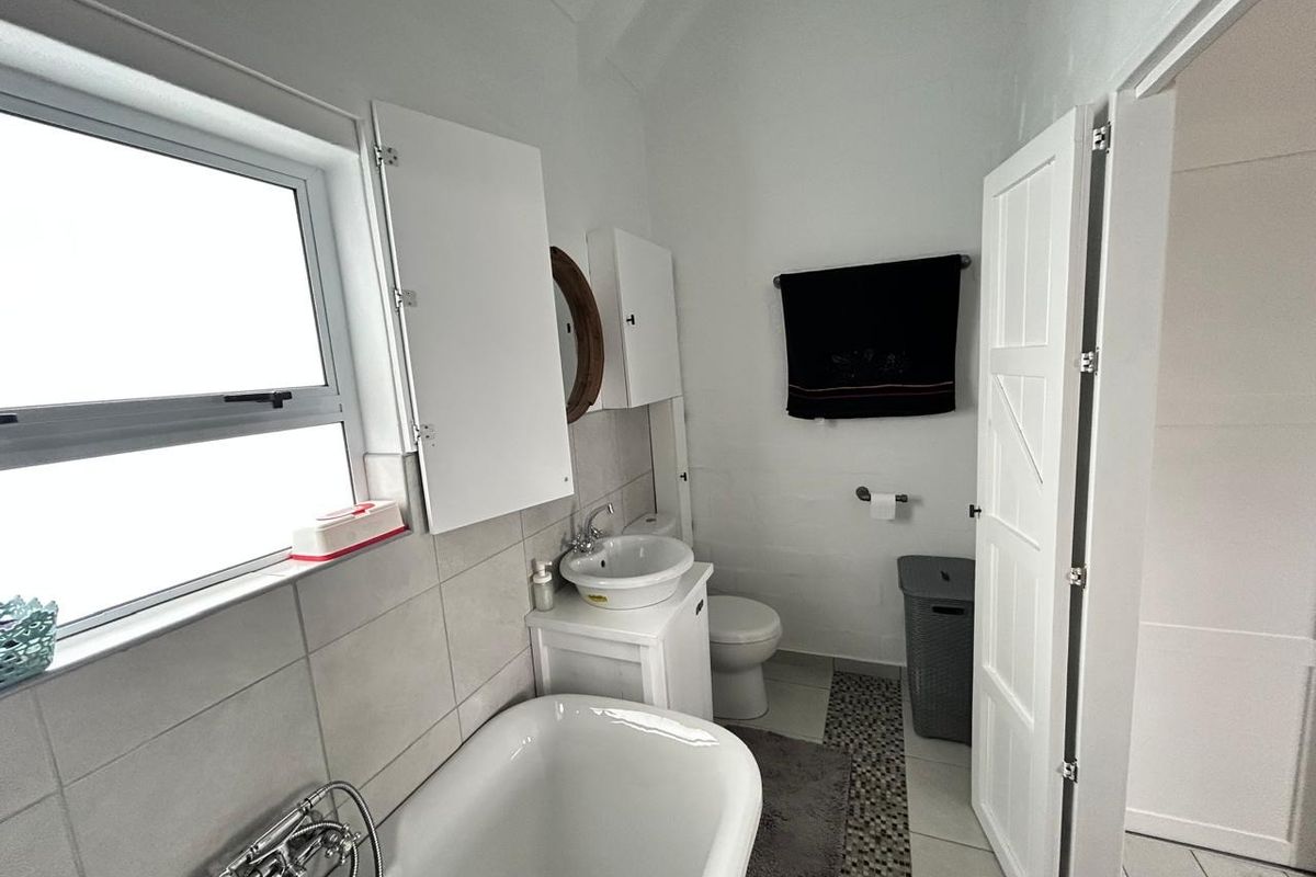 A functional bathroom featuring a freestanding bathtub, vanity basin, toilet, and neutral tiled finishes with natural light from a side window.