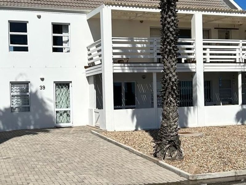 Front elevation of a two-story house featuring a paved driveway, gravel garden, and a covered balcony with white railings.
