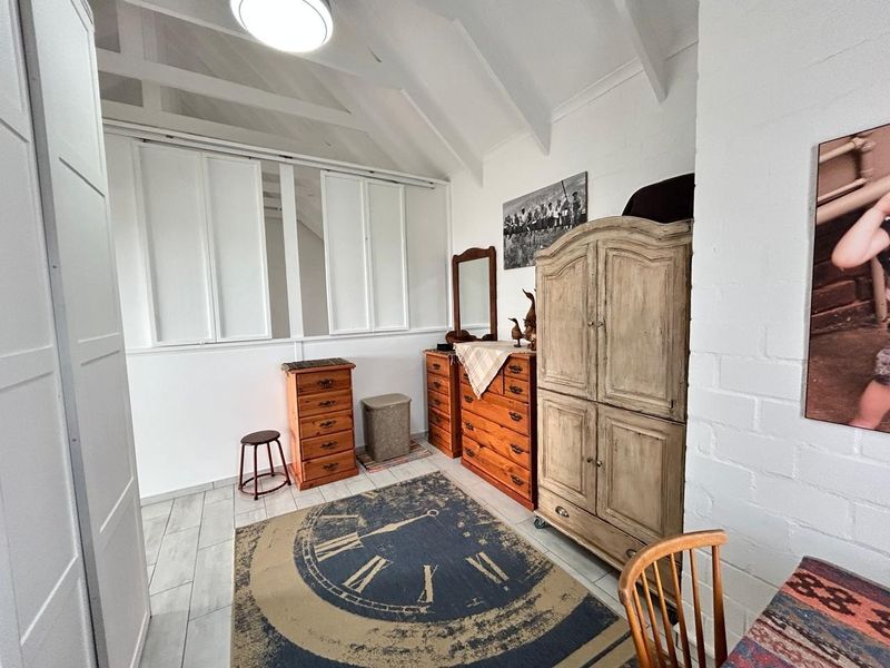 A bedroom featuring a vaulted ceiling with exposed rafters, tiled flooring, and built-in shutters, offering a bright and airy atmosphere.