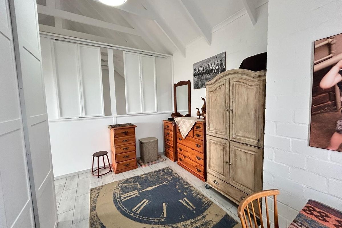A bedroom featuring a vaulted ceiling with exposed rafters, tiled flooring, and built-in shutters, offering a bright and airy atmosphere.