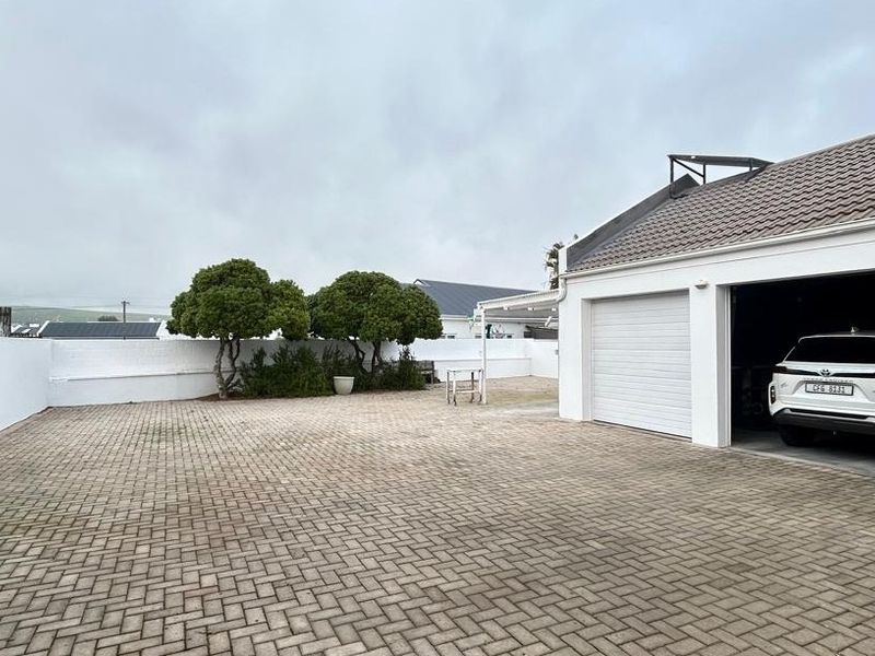 Spacious paved driveway leading to a double garage with a clean exterior facade and perimeter boundary wall.