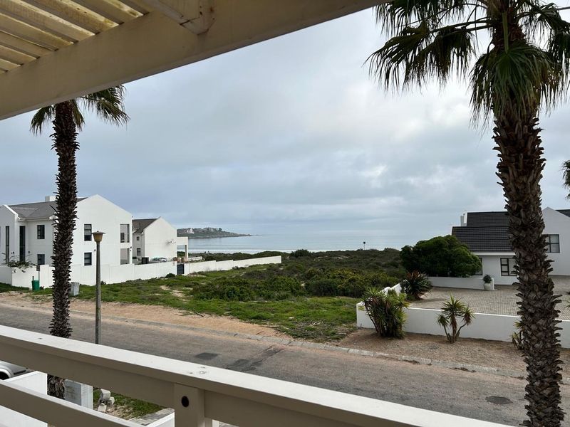 Elevated view of the coastal landscape and surrounding residential neighborhood, captured from a balcony with a white railing and pergola structure.