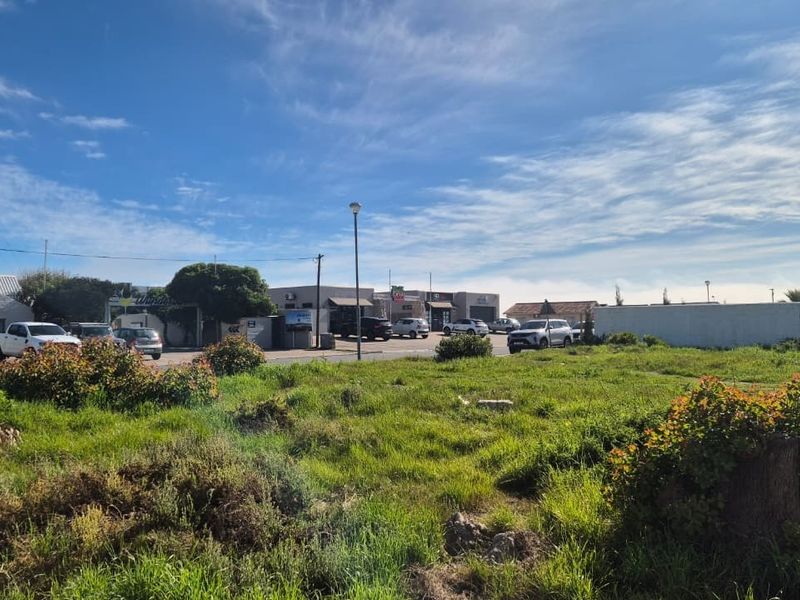A vacant residential plot of land featuring natural grass coverage, situated in a developed area with nearby commercial and residential infrastructure.