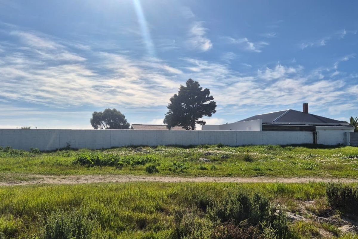 A view of a vacant residential plot featuring a boundary wall and natural grass coverage, suitable for new development.