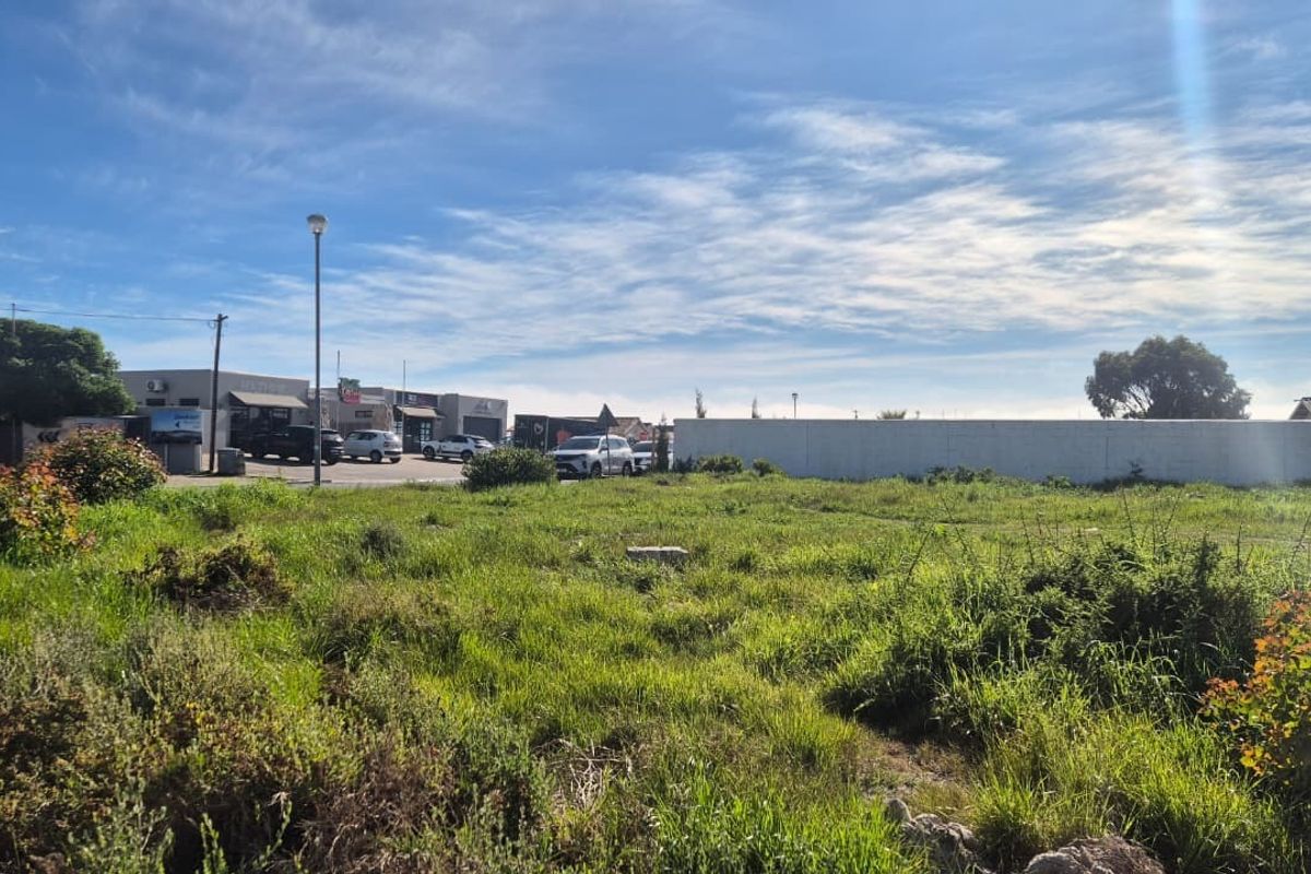 A vacant residential plot of land featuring natural grass coverage, enclosed by a boundary wall, situated in a developed neighborhood setting.