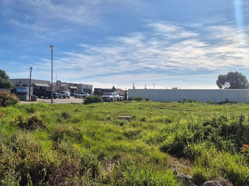 A vacant residential plot of land featuring natural grass coverage, enclosed by a boundary wall, situated in a developed neighborhood setting.