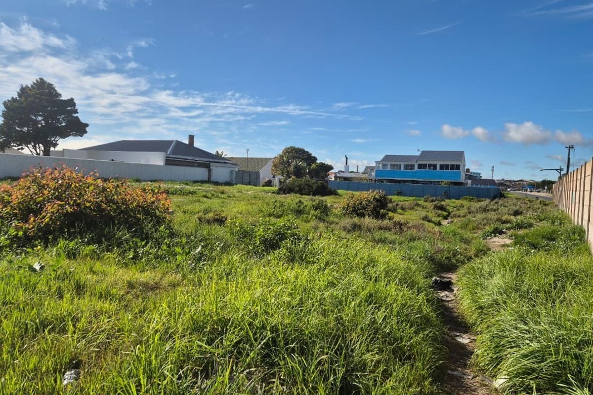 A vacant residential plot featuring overgrown grass and enclosed by precast concrete boundary walls in a developed neighborhood setting.