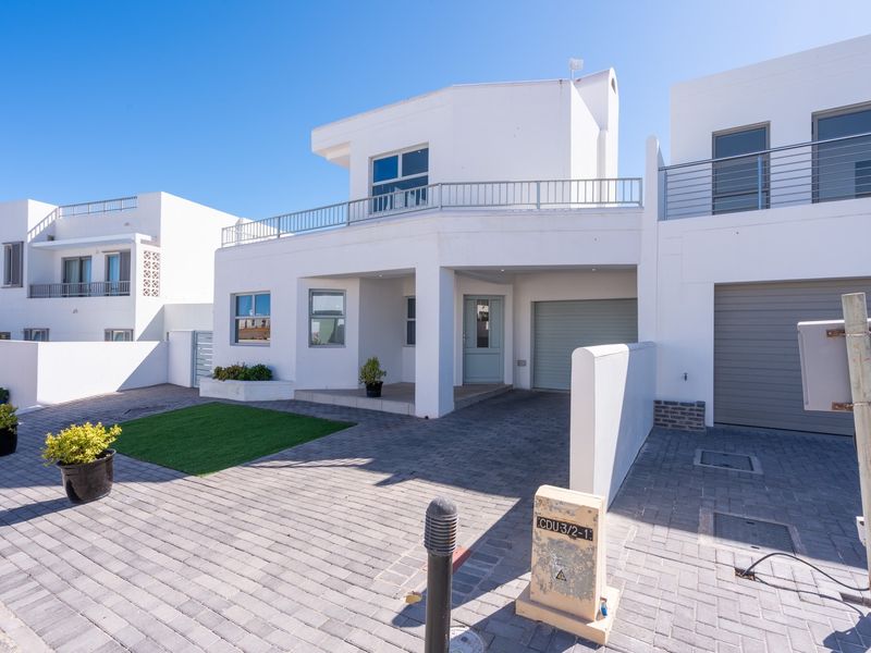 Modern double-story townhouse featuring a paved driveway, integrated garage, and a balcony with metal railings.