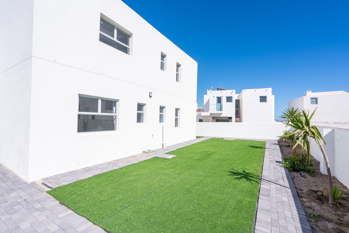 A clean rear exterior view of the property featuring a low-maintenance artificial lawn, paved pathways, and a secure boundary wall.
