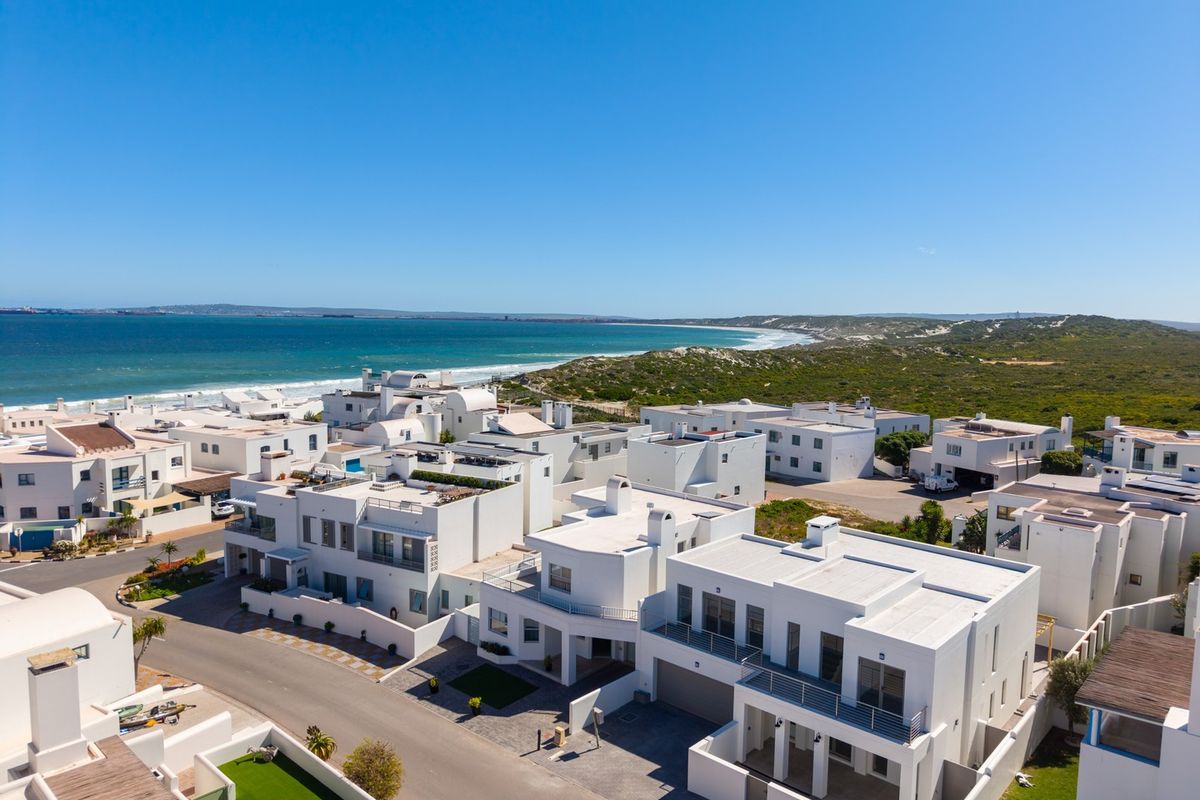 Aerial view of a modern coastal residential estate featuring white architectural homes, paved streets, and proximity to the ocean.