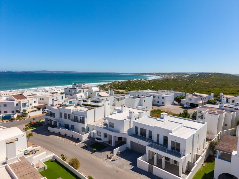 Aerial view of a modern coastal residential estate featuring white architectural homes, paved streets, and proximity to the ocean.