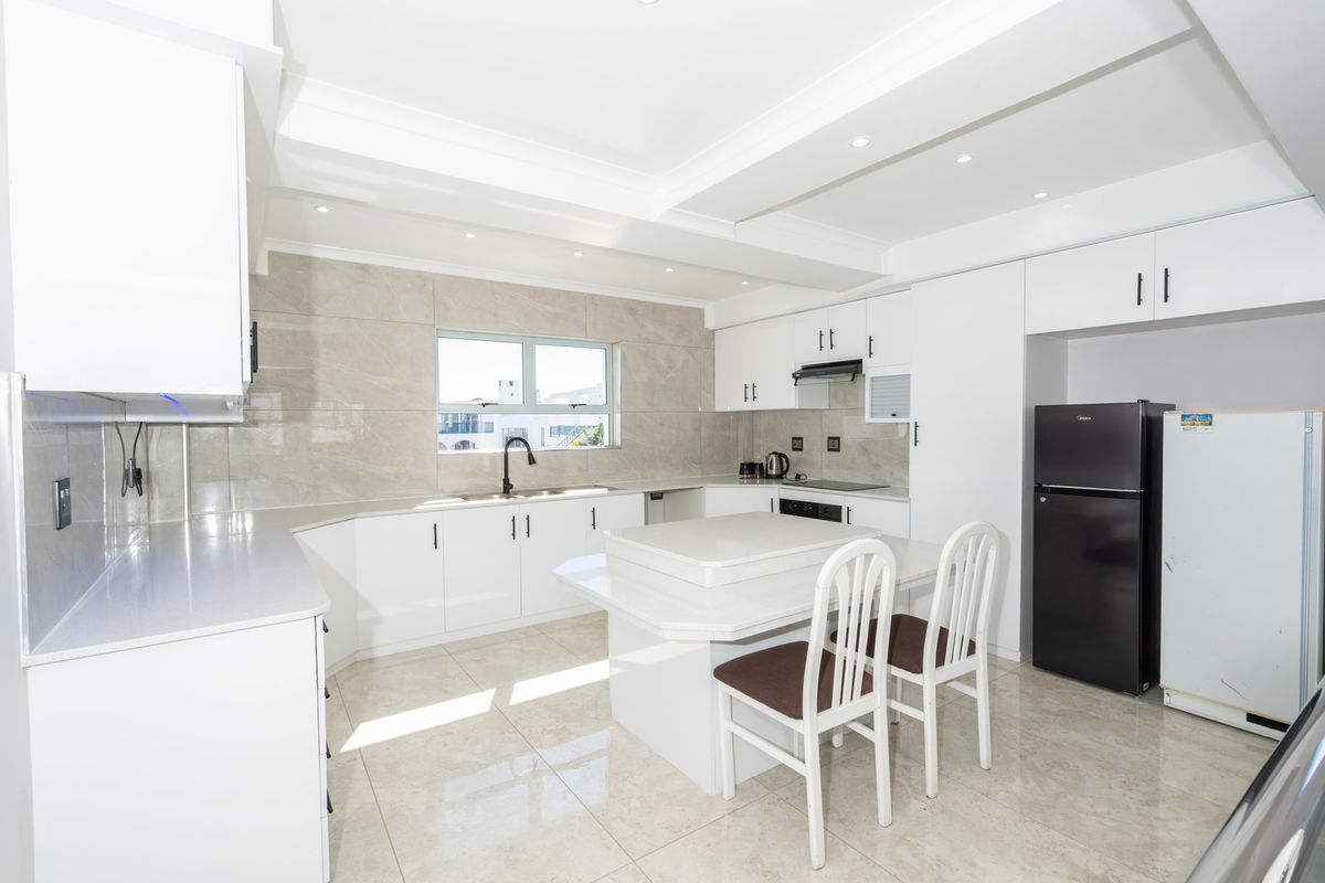 Modern kitchen featuring white cabinetry, stone countertops, tiled backsplash, and integrated appliances with polished tile flooring and recessed lighting.