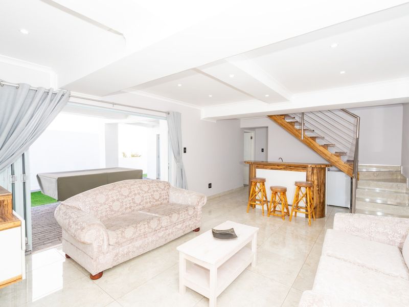 Spacious open-plan living area featuring tiled floors, recessed lighting, a built-in bar, and direct access to the outdoor patio through sliding glass doors.