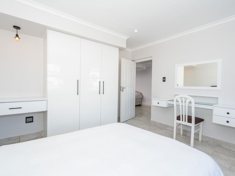 A bright bedroom featuring built-in white cabinetry, a matching vanity unit, tiled flooring, and clean, modern finishes.