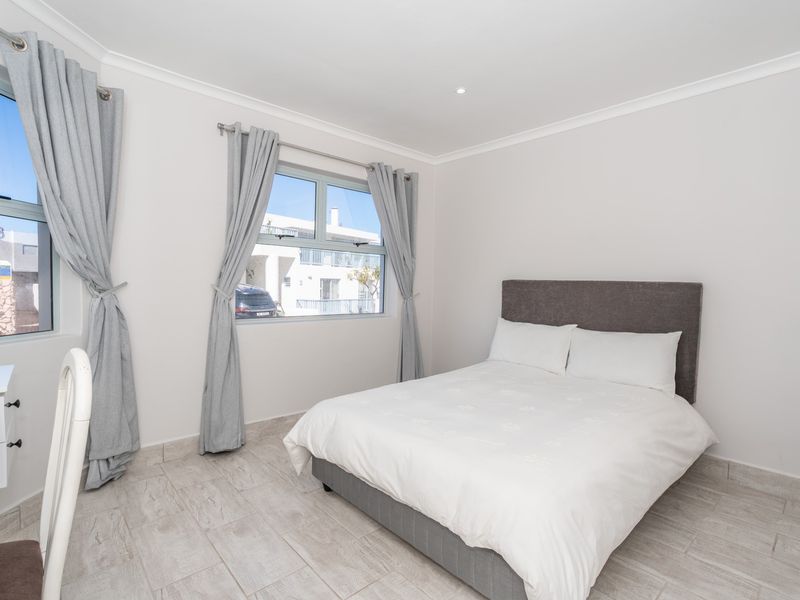 A bright and well-maintained bedroom featuring neutral wall finishes, tiled flooring, and aluminium-framed windows with integrated curtain tracks.