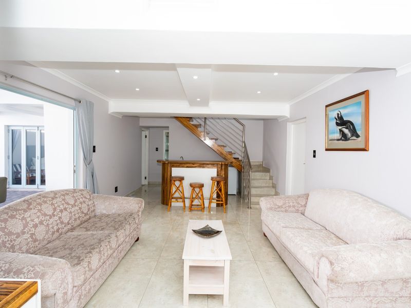 Spacious living area featuring tiled flooring, recessed lighting, a built-in bar, and a staircase with a modern stainless steel balustrade leading to the upper level.
