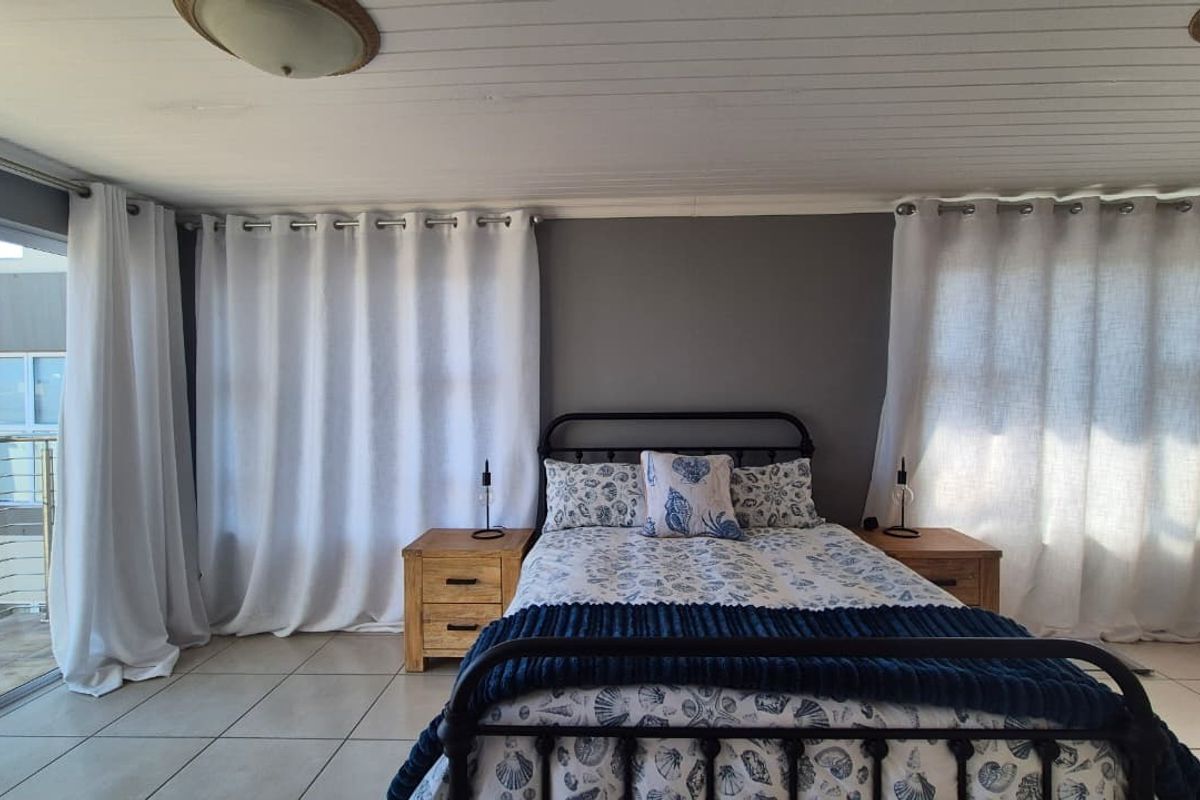 A well-lit bedroom featuring tiled flooring, a tongue and groove ceiling, and a sliding glass door providing access to an outdoor balcony.