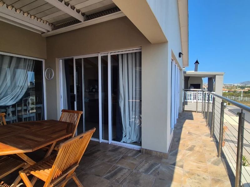 A spacious covered balcony featuring tiled flooring, a stainless steel balustrade, and a built-in braai, offering an ideal space for outdoor entertaining.