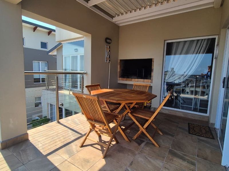 Covered balcony featuring tiled flooring, a built-in braai, and stainless steel railing, offering a functional outdoor entertainment space.