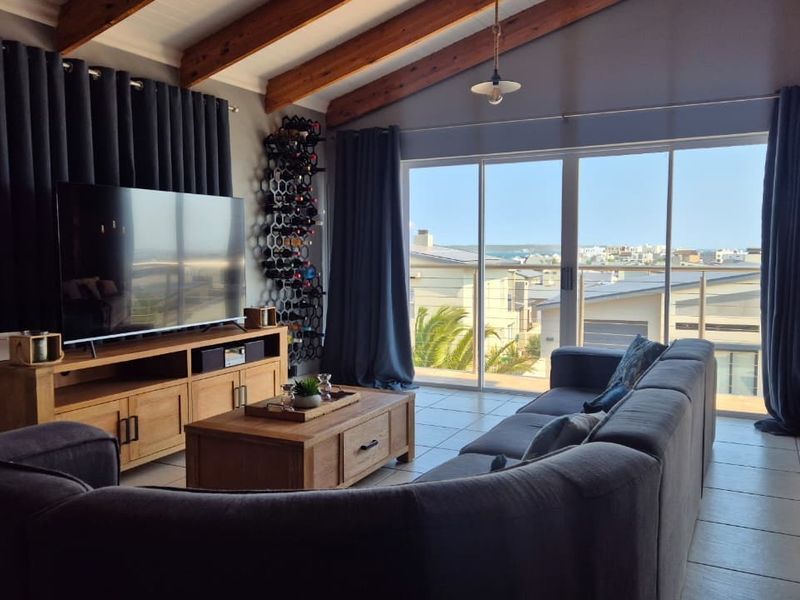 Spacious living room featuring exposed timber ceiling beams, tiled flooring, and large sliding glass doors opening to a balcony with coastal views.