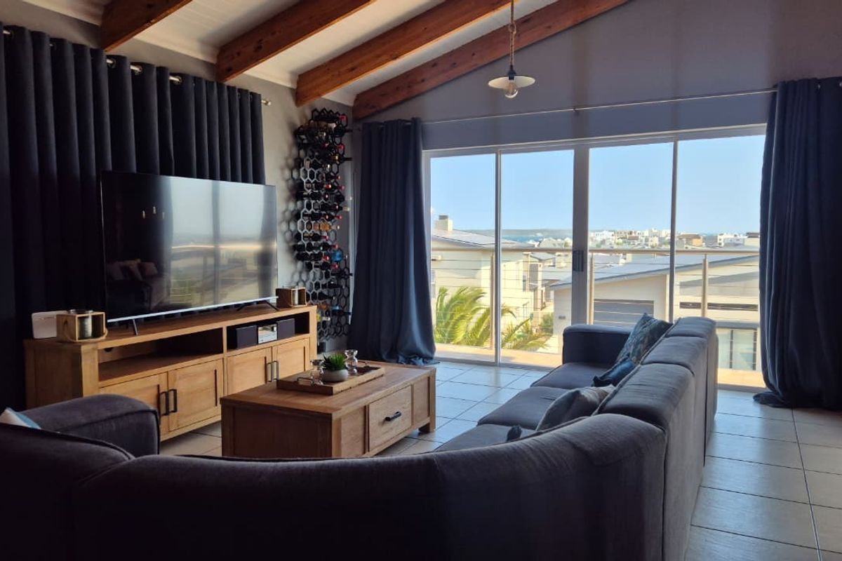 Spacious living room featuring exposed timber ceiling beams, tiled flooring, and large sliding glass doors opening to a balcony with coastal views.