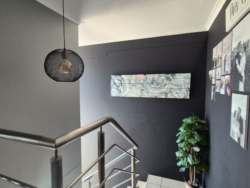A modern hallway featuring a metal balustrade staircase and a contemporary pendant light fixture against dark painted walls.