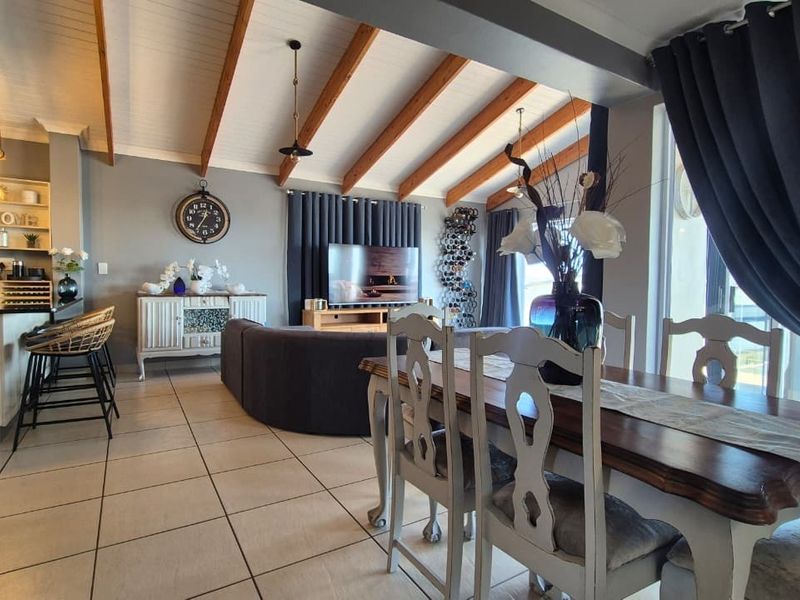 Spacious open-plan living, dining, and kitchen area featuring exposed timber ceiling beams, tiled flooring, and seamless access to outdoor space through sliding glass doors.