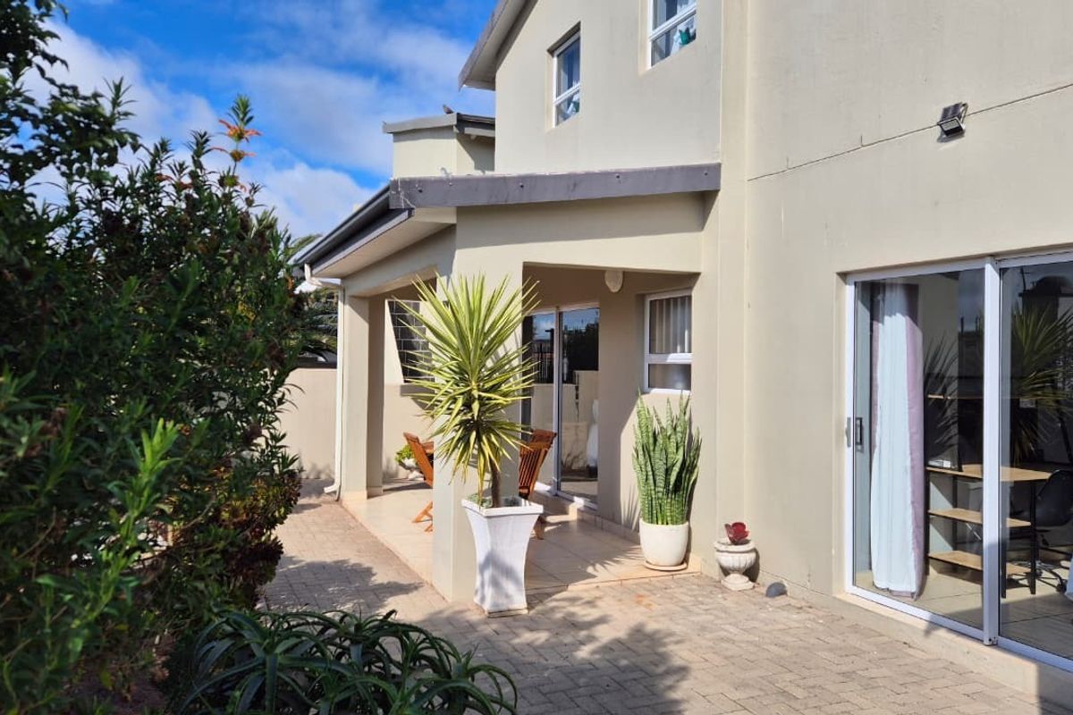 A well-maintained rear exterior view featuring a paved patio area, covered veranda, and sliding glass doors providing access to the home's interior.