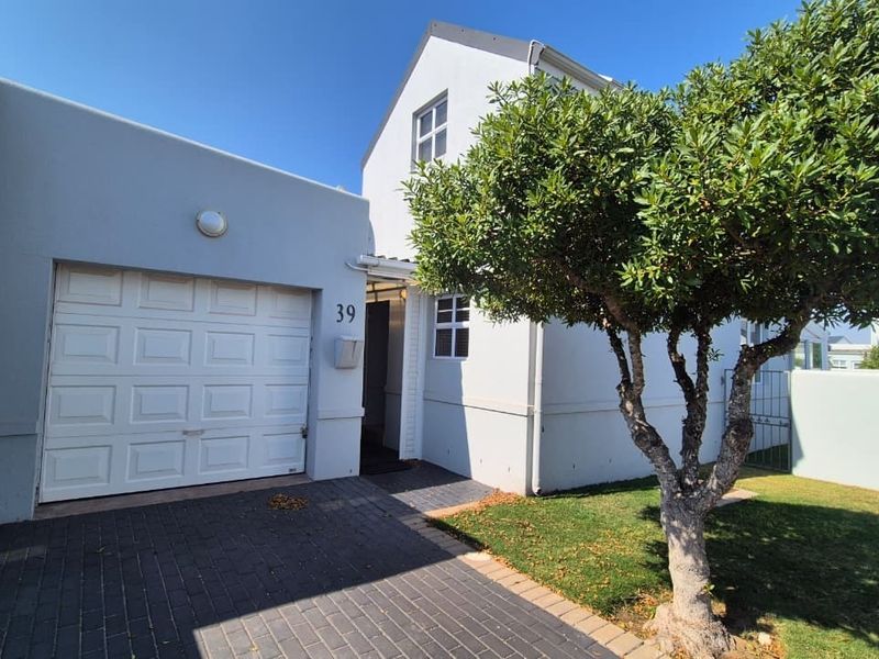 Front elevation of the property featuring a single garage, paved driveway, and a neat entrance area with established landscaping.