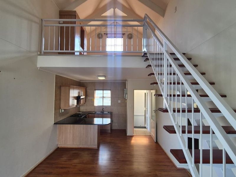 Open plan living area featuring a kitchen with built-in cabinetry, laminate flooring, and a mezzanine level accessed by a staircase.