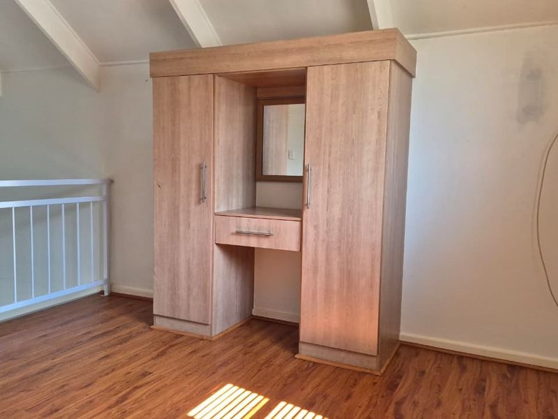 Bedroom loft area featuring laminate flooring, exposed rafters, a built-in wardrobe with vanity, and a metal balustrade overlooking the lower level.