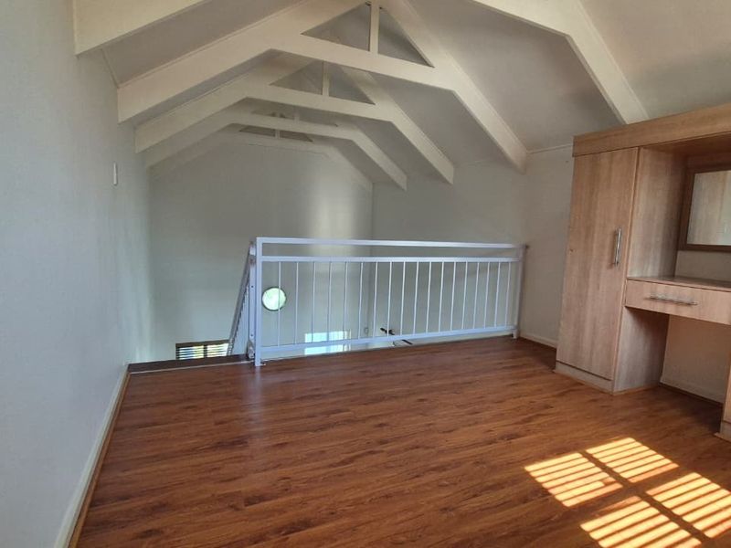 A spacious loft-style bedroom featuring vaulted ceilings with exposed rafters, laminate flooring, and a built-in wardrobe with a vanity area.