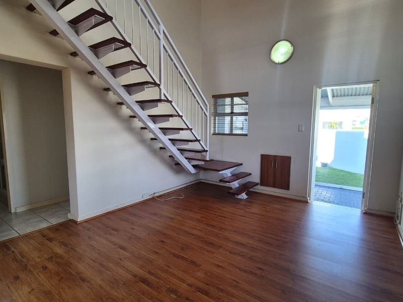 An open-plan living area featuring laminate flooring, a white metal staircase, and direct access to an outdoor patio area.