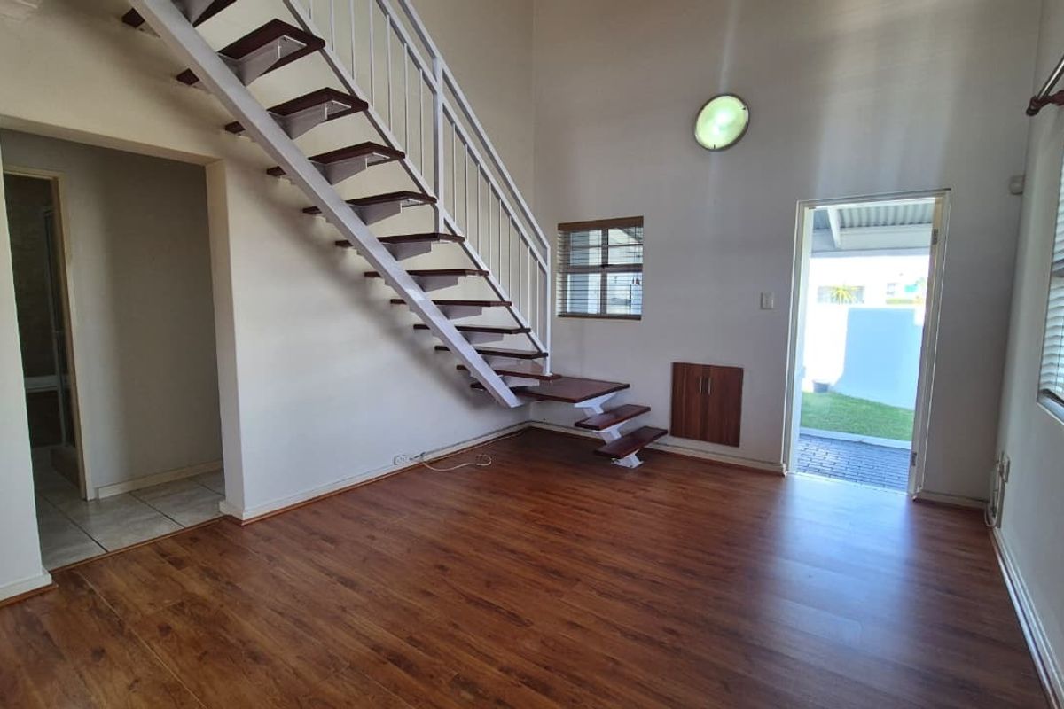 An open-plan living area featuring laminate flooring, a white metal staircase, and direct access to an outdoor patio area.