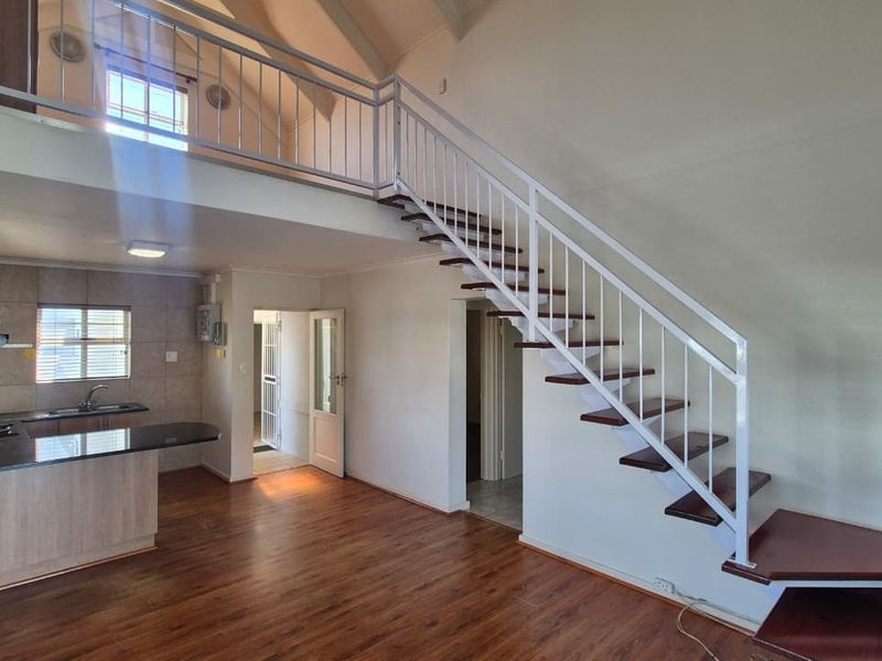 Open-plan living area featuring a modern kitchen with granite countertops, laminate flooring, and a staircase leading to a mezzanine level.