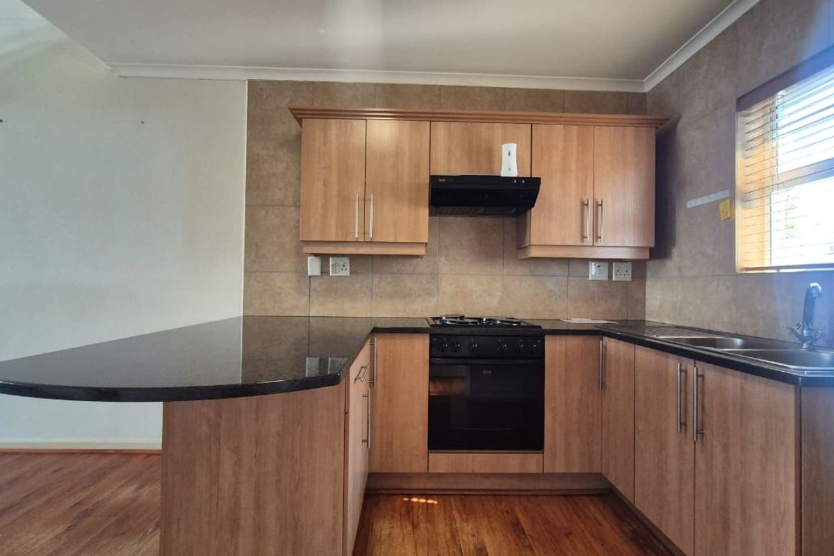 A functional kitchen featuring wood-look laminate cabinetry, granite countertops, a built-in oven with gas hob, and a breakfast bar extension.
