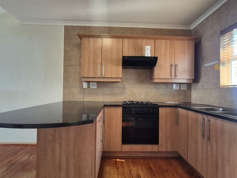 A functional kitchen featuring wood-look laminate cabinetry, granite countertops, a built-in oven with gas hob, and a breakfast bar extension.
