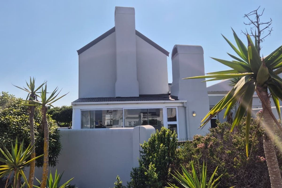 Rear exterior view of the property featuring a prominent chimney, sliding glass doors, and a surrounding boundary wall.
