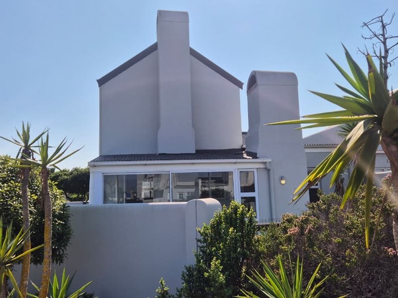 Rear exterior view of the property featuring a prominent chimney, sliding glass doors, and a surrounding boundary wall.