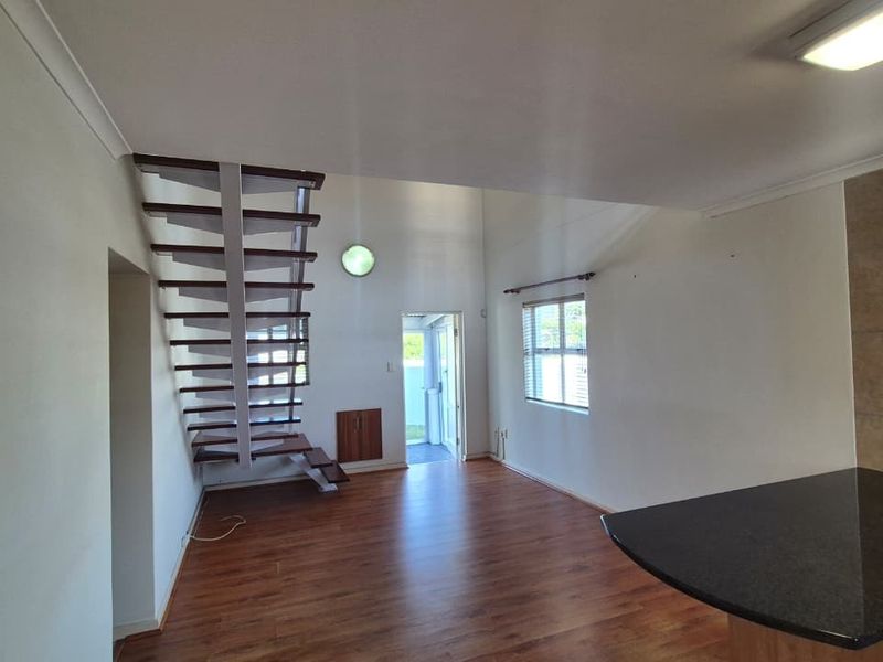 Open-plan living area featuring laminate flooring, a modern open staircase, and a kitchen with granite countertops and built-in cabinetry.