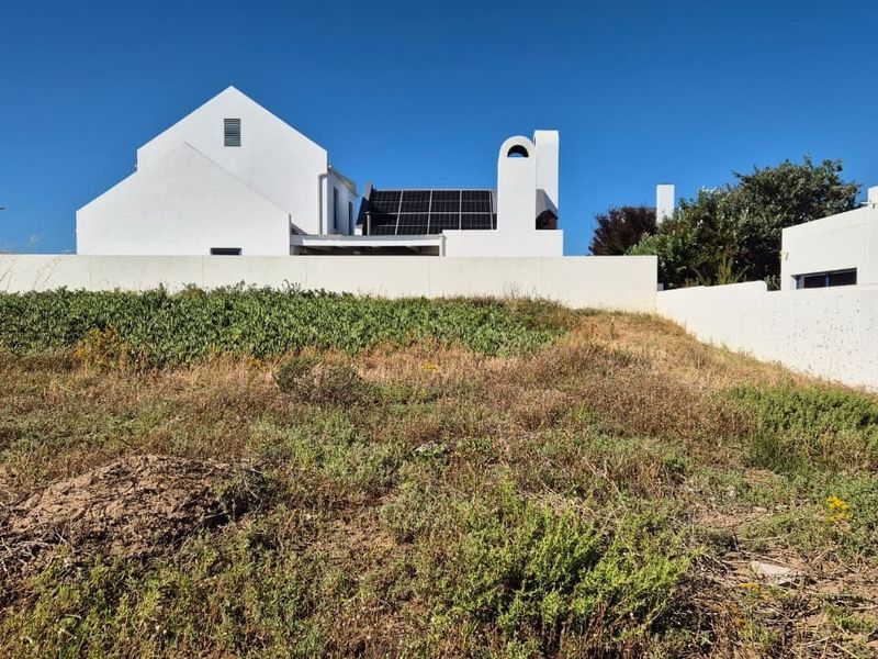 Rear view of a modern white house featuring solar panels, a chimney, and a surrounding boundary wall set against a natural landscape.