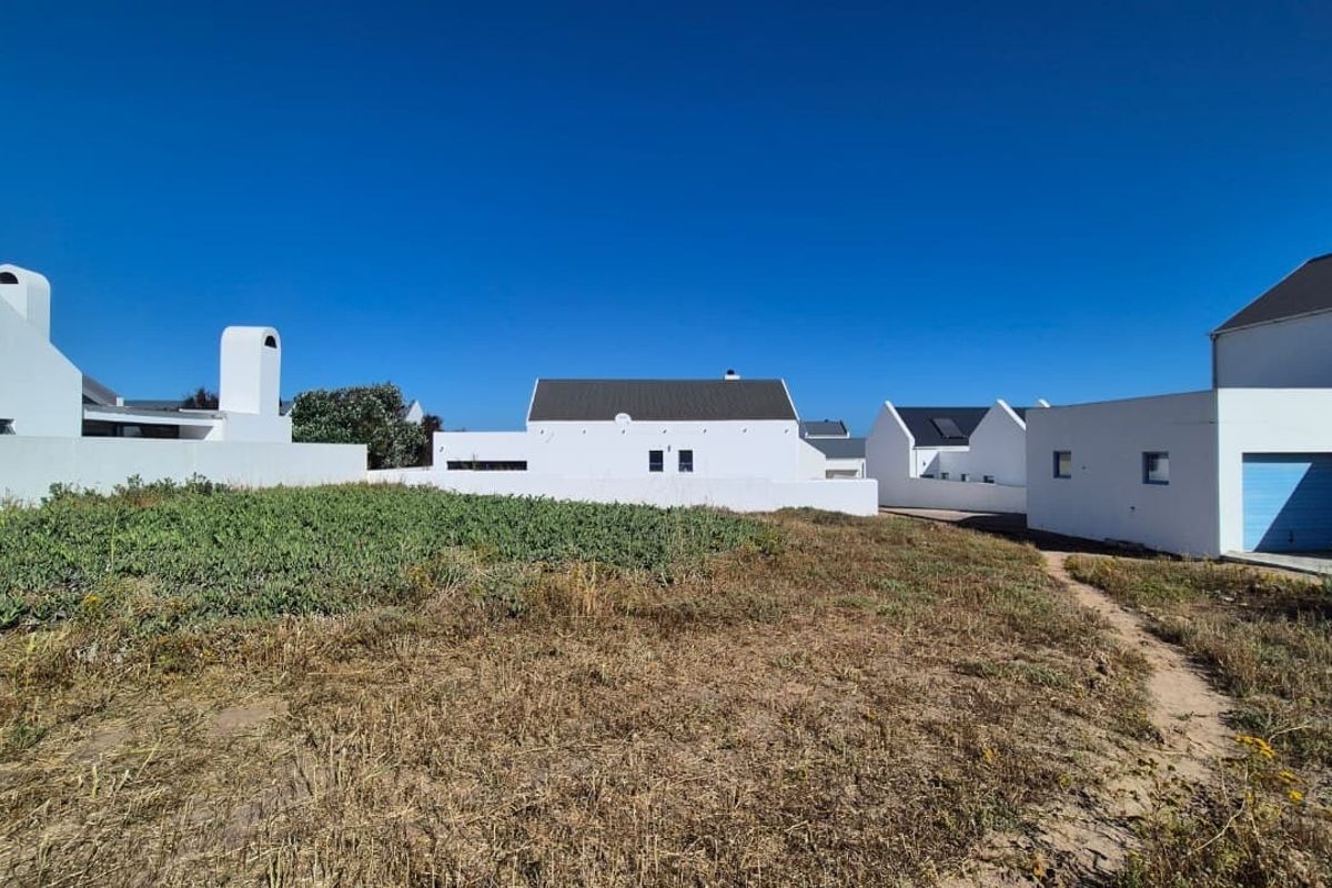 Rear view of a white-walled residential property featuring a pitched roof, chimney, and garage access, set against a natural, unlandscaped outdoor area.