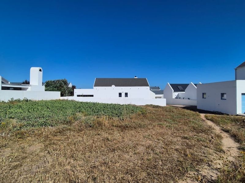 Rear view of a white-walled residential property featuring a pitched roof, chimney, and garage access, set against a natural, unlandscaped outdoor area.