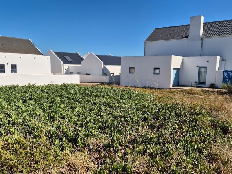 Rear view of a white residential house featuring a corrugated metal roof, chimney, and surrounding garden area with established ground cover.