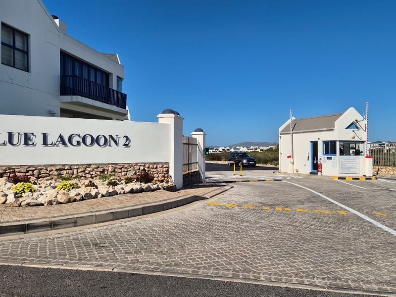 The entrance to Blue Lagoon 2 estate featuring a secure gatehouse, paved driveway, and prominent estate signage.